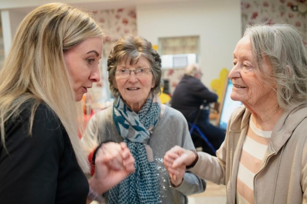 Home care aide visiting and laughing with two senior women in a bright living room