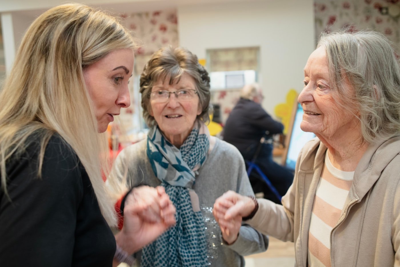 Home care aide visiting and laughing with two senior women in a bright living room